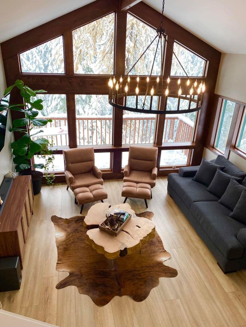 Modern living room with large windows, cozy seating, and a stylish chandelier in a snowy setting.