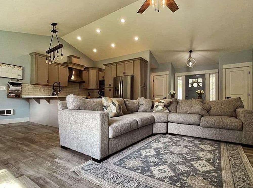 Modern living room with gray sectional couch, decorative rug, and open kitchen design.