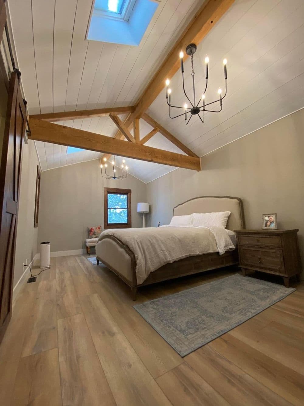 Cozy bedroom with vaulted ceiling, wooden beams, chandelier, and elegant decor.
