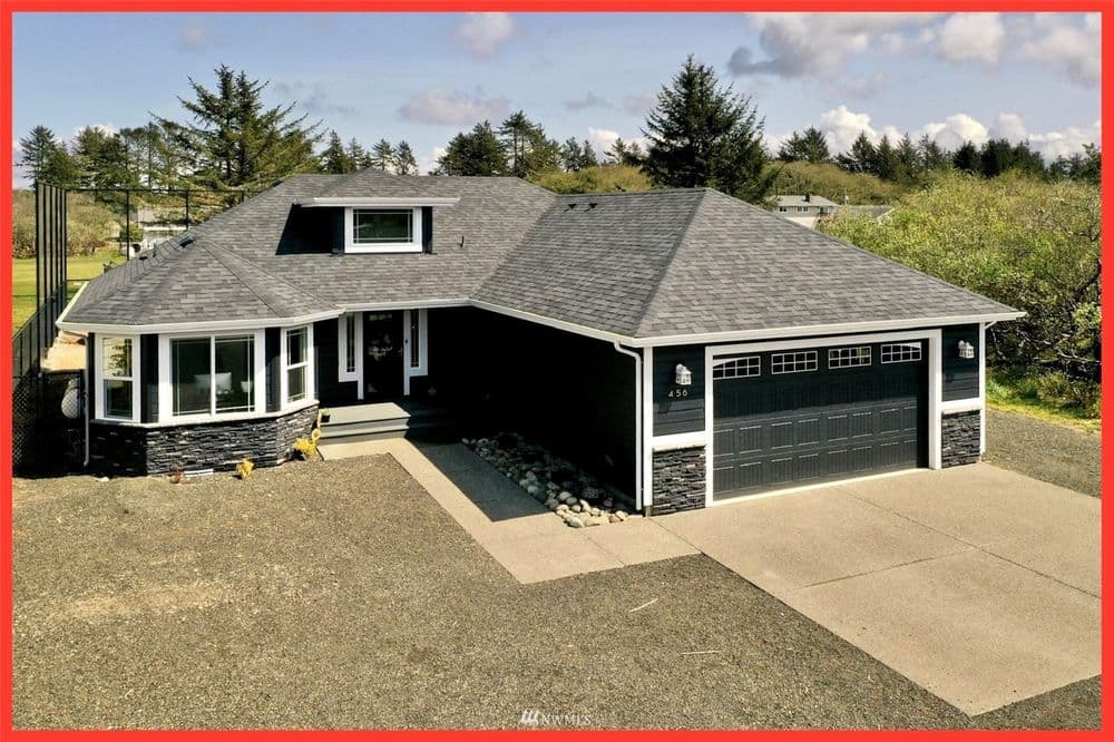 Modern black and stone exterior home with garage and landscaped driveway.