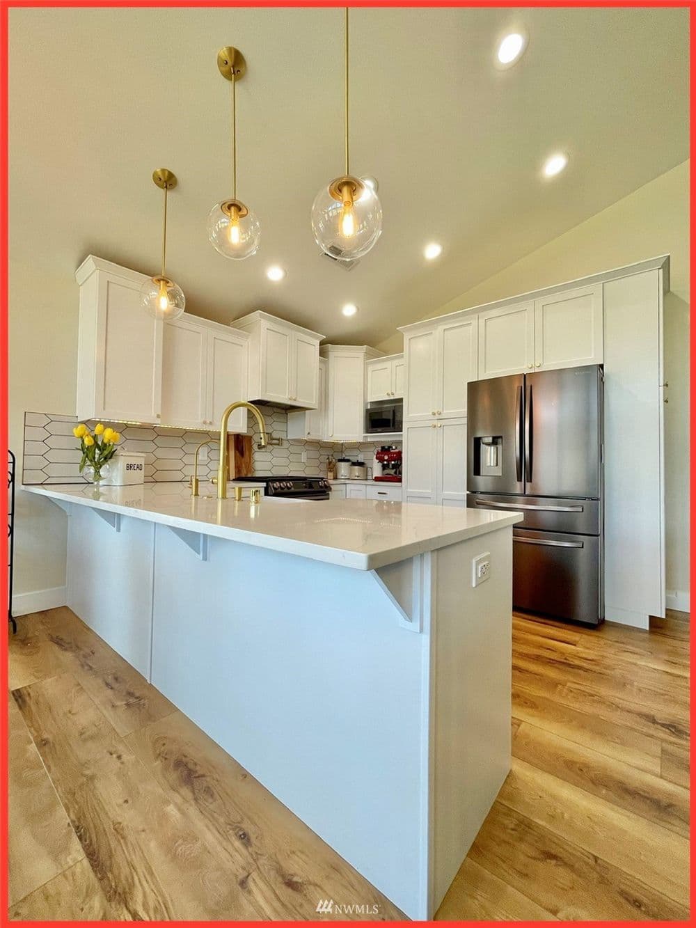 Modern kitchen with white cabinets, quartz island, stainless steel appliances, and pendant lighting.