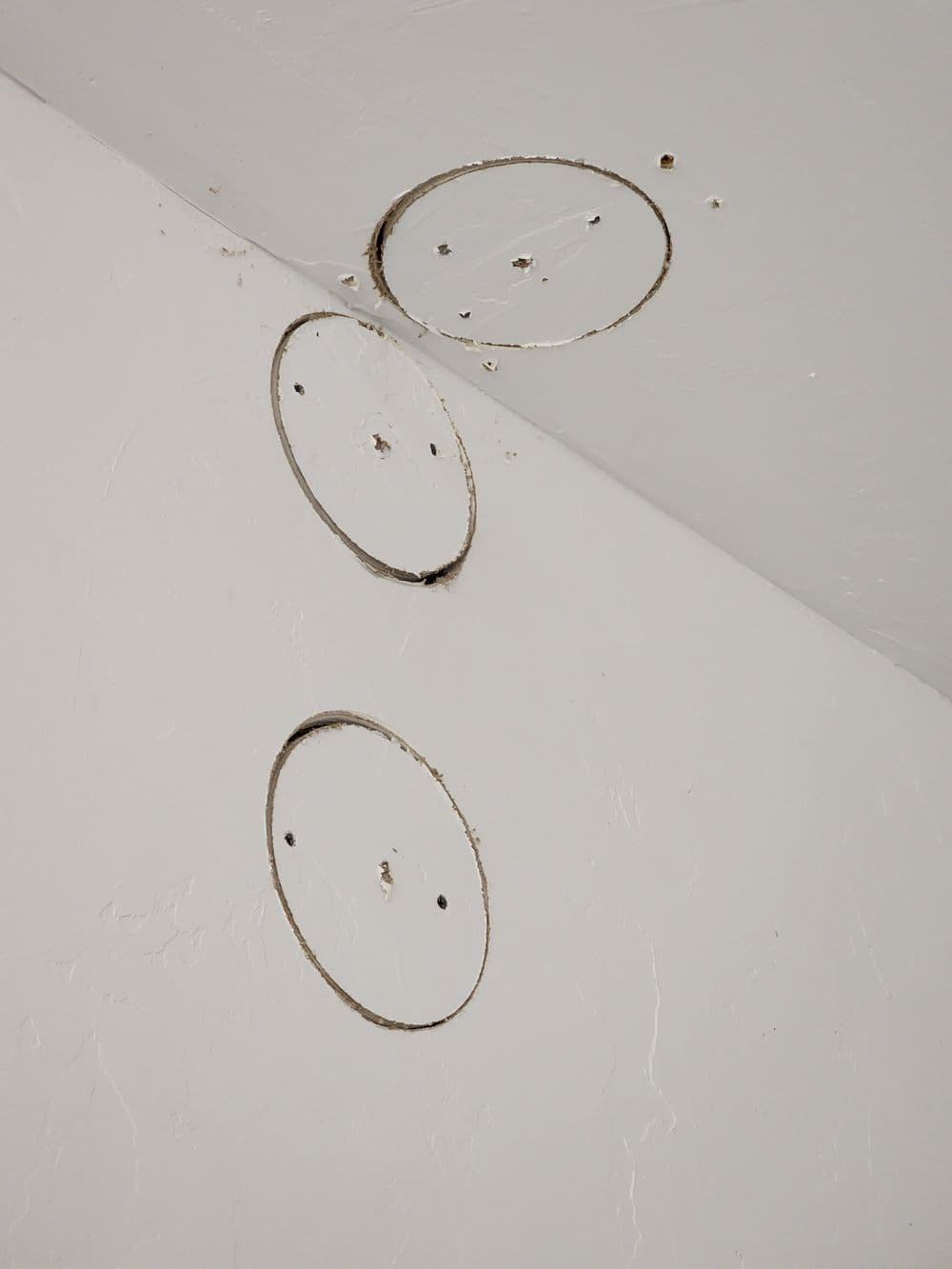 Ceiling with three circular cutouts and visible texture, showing repair or installation work.