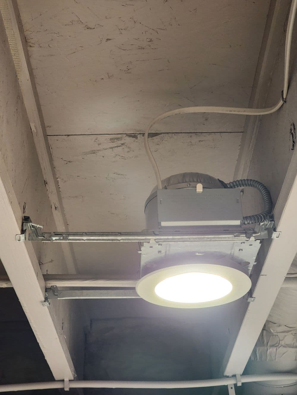 Ceiling-mounted LED light fixture with wiring in a basement setting.