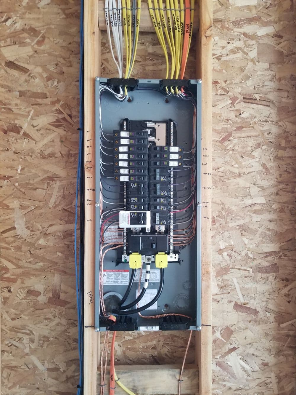 Electrical panel with circuit breakers and connected wiring in a residential construction setting.